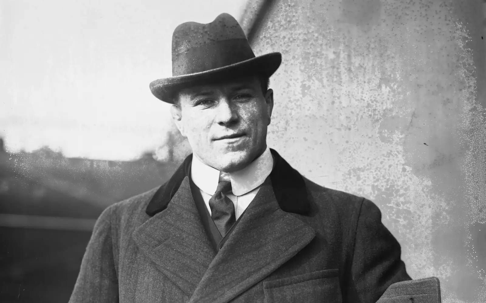 Black-and-white portrait of George Hackenschmidt in a felt hat, wing collar, tie and heavy overcoat, smiling slightly