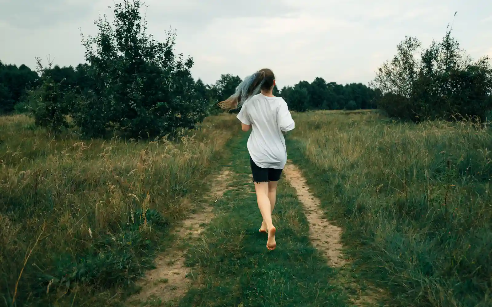 A person seen from behind jogging along a grassy two-track path through a green meadow