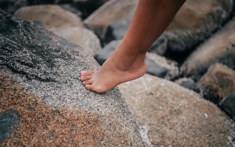 A bare foot stepping onto a smooth granite rock beside darker boulders
